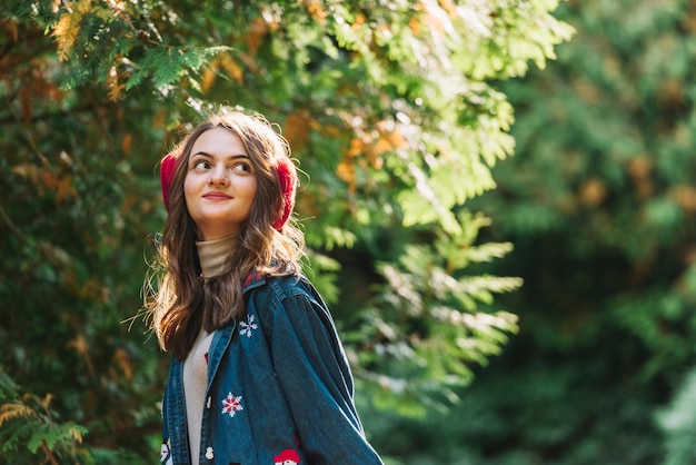 Young woman in earmuffs near green twigs