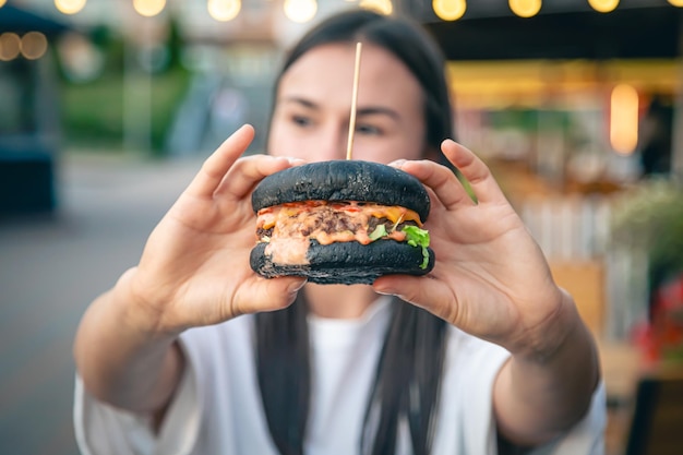 Free photo a young woman eating burger in street cafe