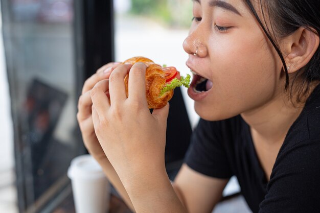 Young woman eating croissant sandwiches in office room