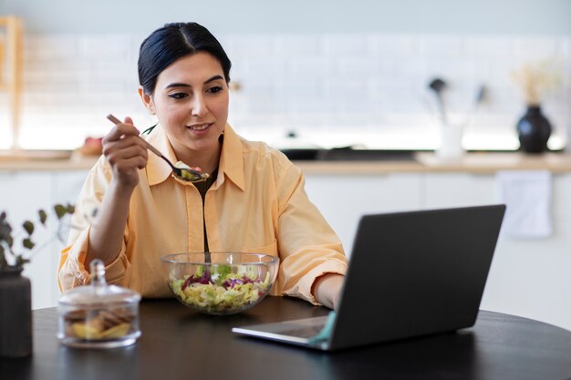 Young woman eating salad and watching video