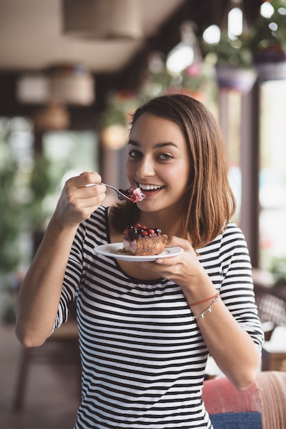 Free photo young woman eating strawberry cheesecake