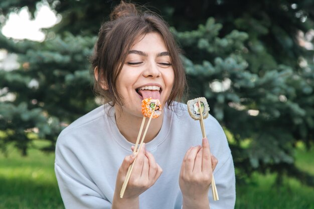 A young woman eating sushi in the park picnic in nature