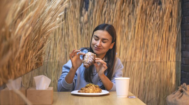 A young woman eats croissants with coffee in a cafe