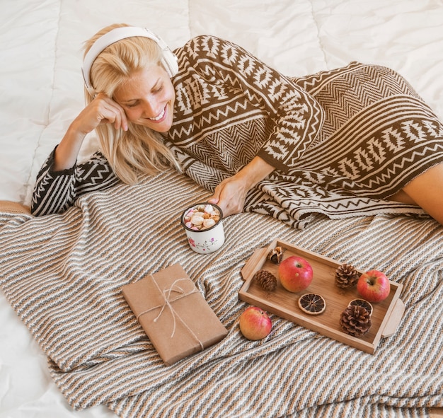 Free photo young woman enjoying music and hot beverage on bed