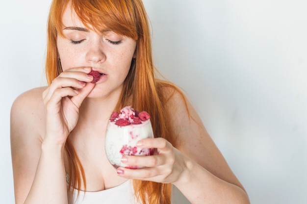 Young woman enjoying raspberries in yogurt smoothie on white background