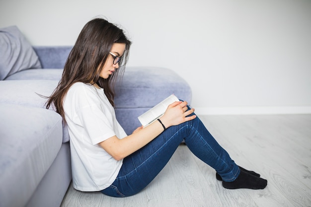 Free Photo young woman enjoying reading near sofa