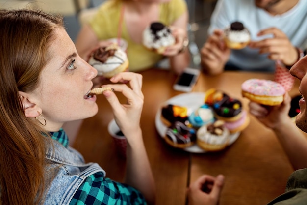 Free photo young woman enjoying while eating donuts with friends