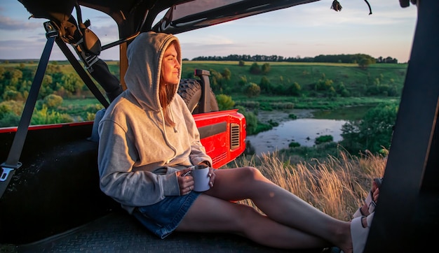 Free photo a young woman enjoys the sunset while sitting in the trunk of an suv