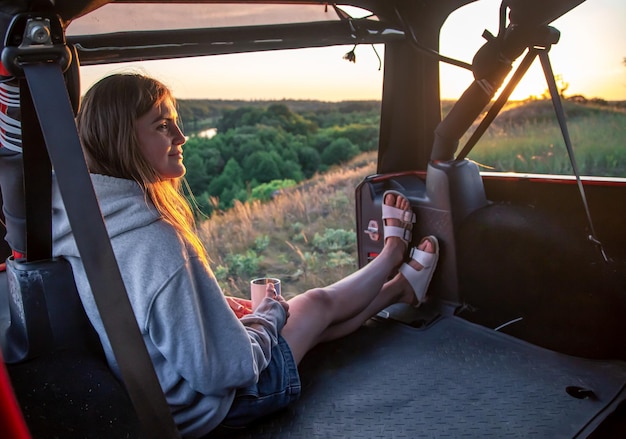 Free photo a young woman enjoys the sunset while sitting in the trunk of an suv