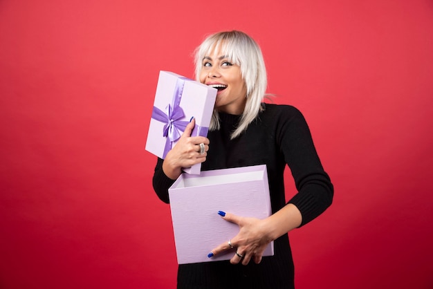 Young woman excited about a present on a red wall. 