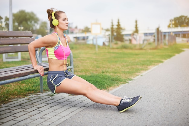 Young woman exercising outdoor. Woman stretching at the bench in the park