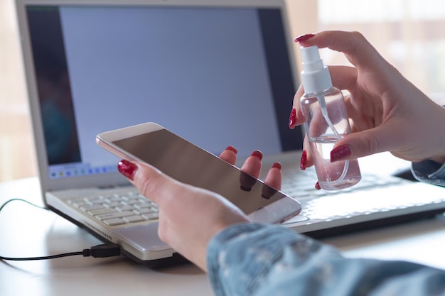 Free photo young woman in face mask disinfecting gadgets surfaces on her workplace