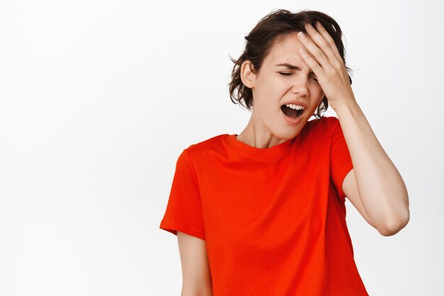 Young woman feeling pain, headache, touching forehead and grimacing from discomfort, feel sick, standing in tshirt on white