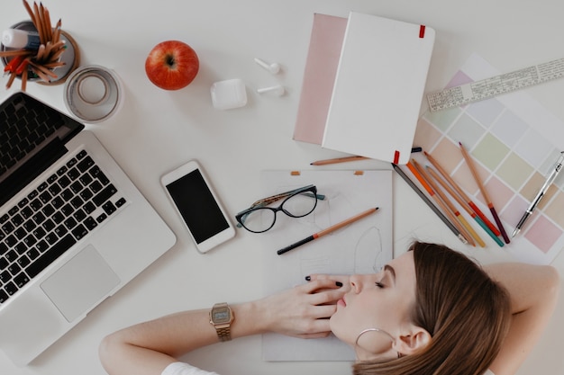 Free photo young woman fell asleep on desktop, surrounded by documents, notes, ruler and devices