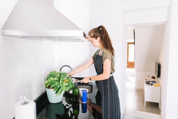 Free photo young woman filling water in sauce pan in the kitchen