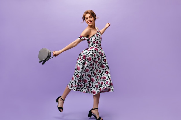 Young Woman in floral dress holds handbag and jumps. Attractive cute young lady with stylish hairstyle in summer outfit posing.