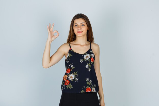 Young woman in floral top showing ok gesture and looking pleased