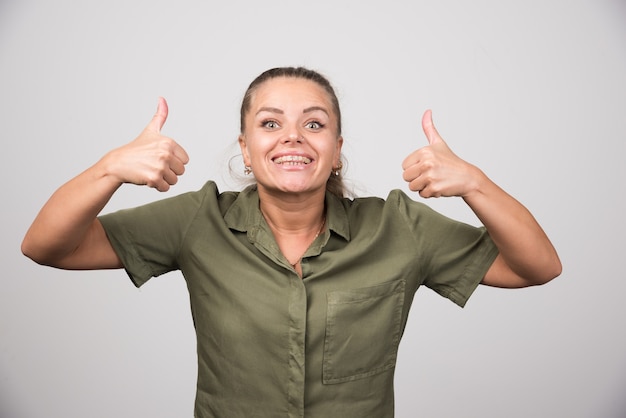 Young woman giving thumbs up on gray wall.