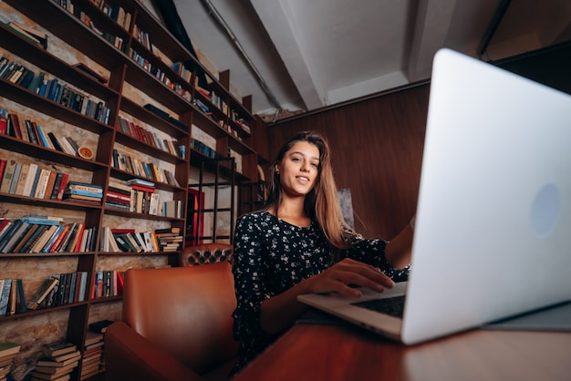 Young woman in glasses works at the laptop while sitting at table