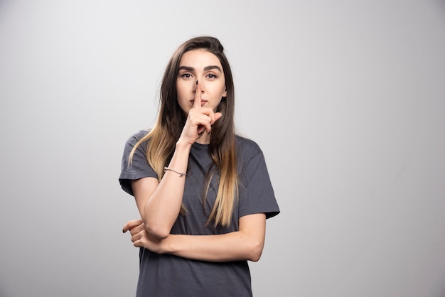 Young woman over a gray background showing a sign of silence gesture putting finger in mouth.