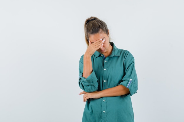 Young woman in green blouse covering forehead with hand and looking serious