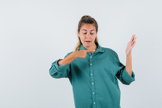 Young woman in green blouse pointing at hand and looking cute