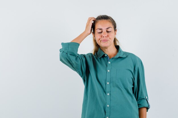 Young woman in green blouse scratching head and looking pensive