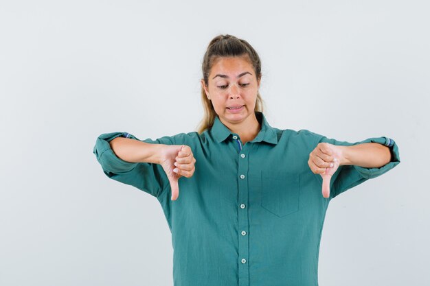 Young woman in green blouse showing thumbs down and looking displeased