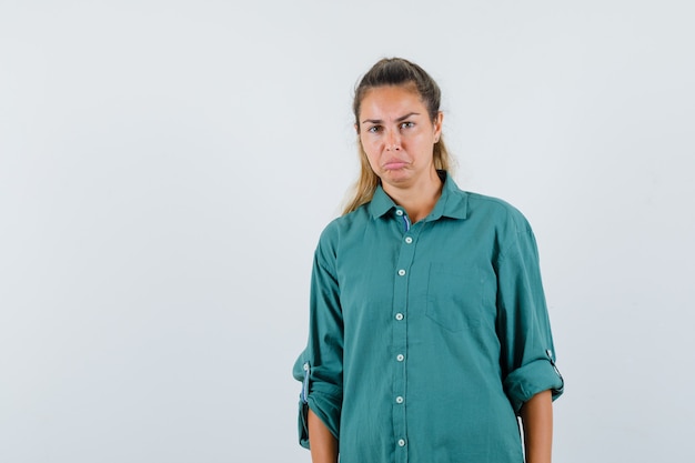 Young woman in green blouse standing straight and posing at front and looking displeased