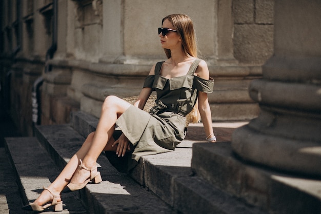 Free photo young woman in green dress sitting on the stairs of an old building