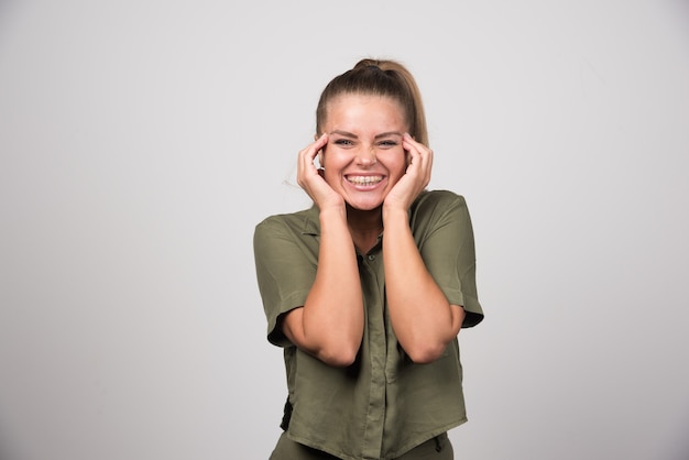 Young woman in green outfit smiling on gray wall.