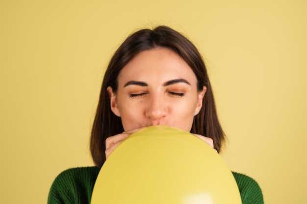 Free photo young woman in green warm sweater blowing air balloon