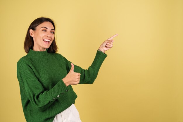 Young woman in green warm sweater pointing fingers to right