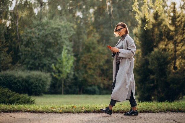 Young woman in grey coat talking on the phone in park