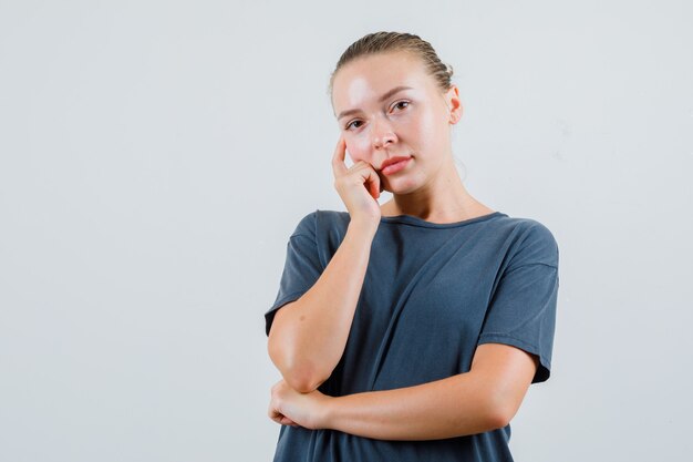 Young woman in grey t-shirt leaning cheek on hand and looking pensive