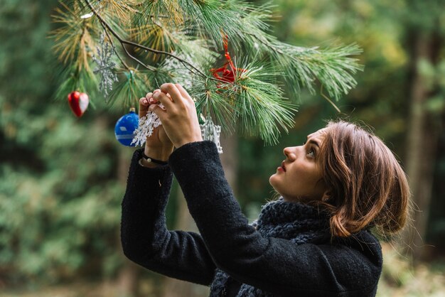 Young woman hanging Christmas toys on twig in forest