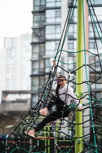 Young woman having fun on the rope pyramid on the playground