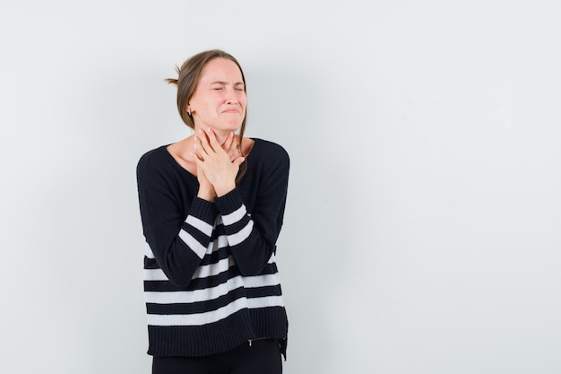 Free photo young woman having sore throat in striped knitwear and black pants and looking exhausted