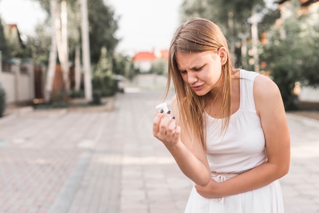 Young woman having stomach ache holding white pills bottle