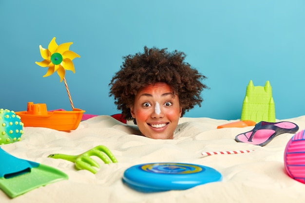 Young woman head with sunscreen cream on face surrounded by beach accessories