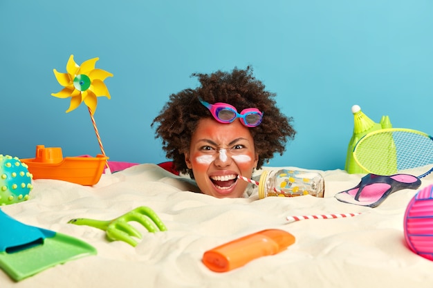 Young woman head with sunscreen cream on face surrounded by beach accessories