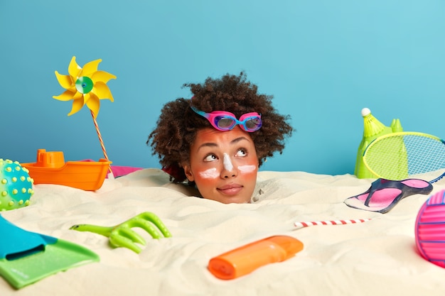 Free Photo young woman head with sunscreen cream on face surrounded by beach accessories