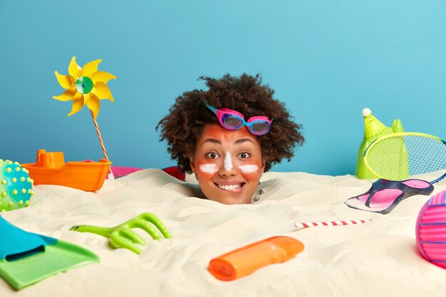 Young woman head with sunscreen cream on face surrounded by beach accessories