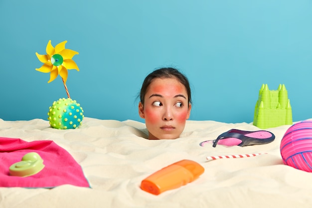 Free photo young woman head with sunscreen cream on face surrounded by beach accessories