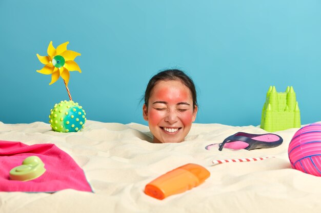 Young woman head with sunscreen cream on face surrounded by beach accessories