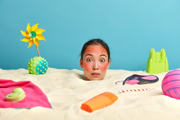 Free photo young woman head with sunscreen cream on face surrounded by beach accessories