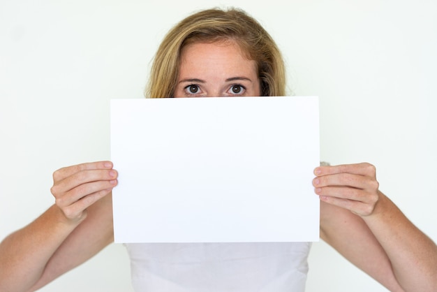 Young woman hiding behind blank sheet of paper