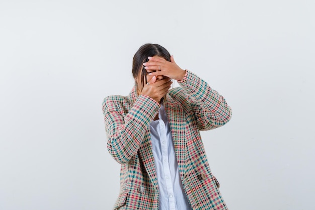 Young woman hiding her face with hands on white background