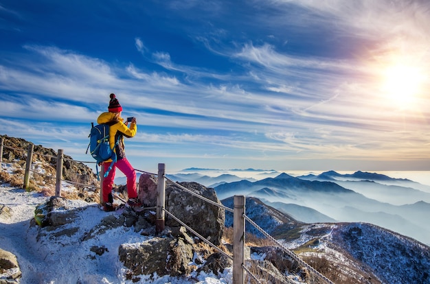 Free Photo young woman hiker taking photo with smartphone on mountains peak in winter