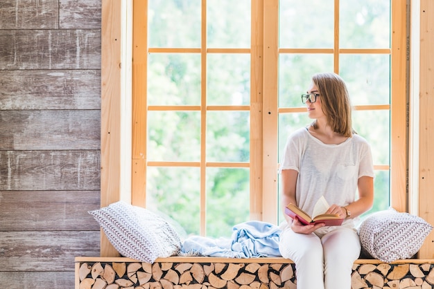 Free photo young woman holding book sitting near the window